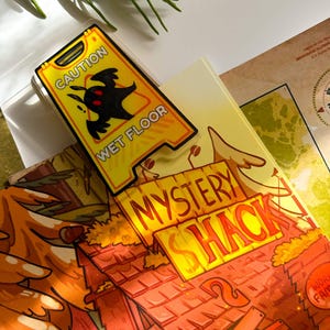 May include: A yellow "Caution Wet Floor" sign with a black silhouette of a creature. The sign is placed on top of a book with the words "Mystery Shack" in orange. A sprig of rosemary is in the background.