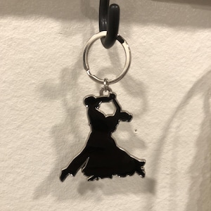 以下が含まれることがあります： ボールルームダンスのポーズをとった2人のダンサーのシルエットが描かれた、黒い金属製のキーホルダーです。