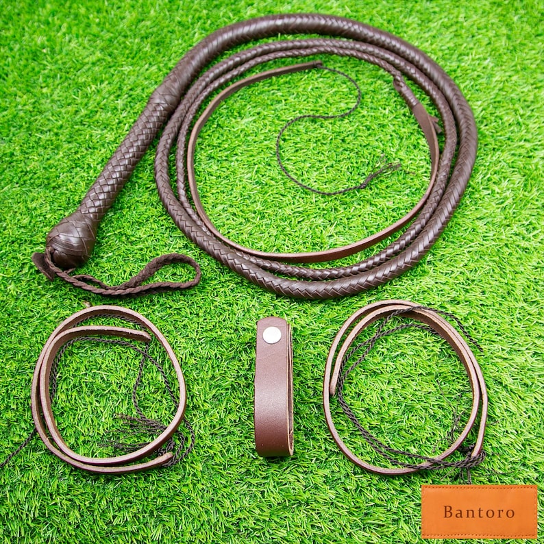 May include: A dark brown leather whip with a braided handle and multiple strands, along with two leather loops and a leather strap. The items are arranged on a green surface. The word "Bantoro" is printed on a small orange rectangle.