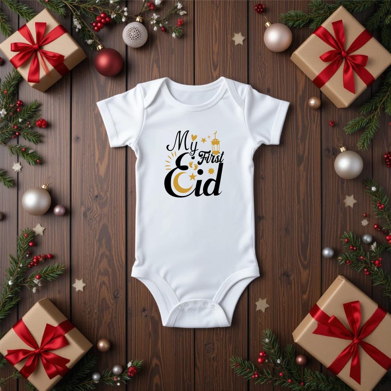 Pu&ograve; includere: Body bianco per neonato con testo nero che recita "My First Eid" con un grafico di luna crescente dorata, stelle e lanterna.