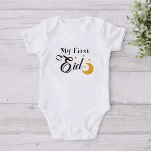 Pu&ograve; includere: Body bianco per neonato con testo nero che recita "My First Eid" con una mezzaluna dorata e stelle.