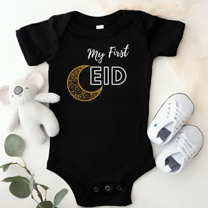 Pu&ograve; includere: Body nero per neonato con una mezzaluna dorata e il testo "My First Eid" in bianco.