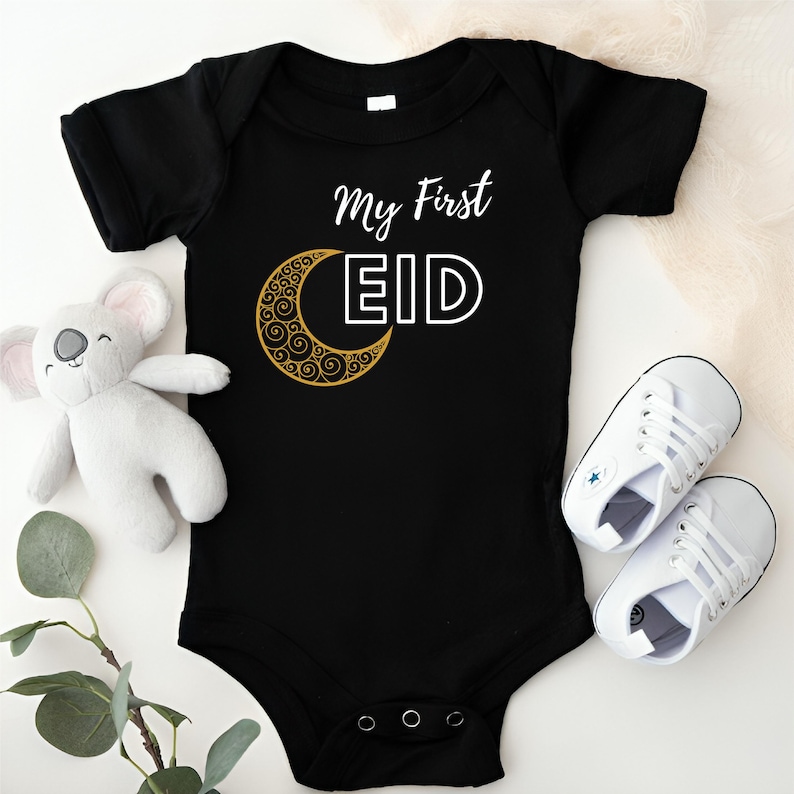 Pu&ograve; includere: Body nero per neonato con una mezzaluna dorata e il testo "My First Eid" in bianco.
