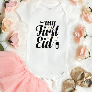 Pu&ograve; includere: Body bianco per neonato con testo nero che recita "my first Eid" con stelle dorate e un'immagine di lanterna dorata.