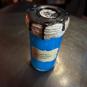 May include: A blue glass roller bottle with a black top and a label that reads "D20 Potion Roller". The top is decorated with a skull design. The bottle is wrapped with twine.