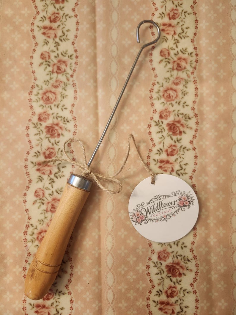 May include: A metal hook tool with a cylindrical wooden handle and a silver-colored metal ferrule. A piece of jute twine is tied around the handle, attaching a round white paper tag printed with the text Wildflower Cottage and floral graphics.