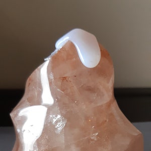 Può includere: Un grande cristallo trasparente, rosa e arancione con una cima bianca, opaca, liscia e arrotondata. Il cristallo ha una forma geometrica sfaccettata.