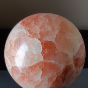 May include: A large, spherical gemstone in pink and white, displayed on a dark wooden stand. The orb has a textured surface with visible crystalline patterns. The gemstone's diameter is approximately 10 cm.