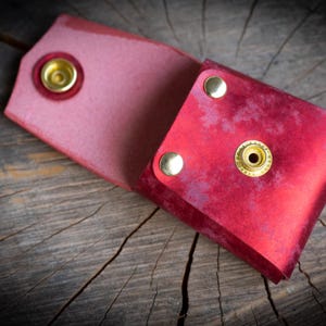 K&ouml;nnte beinhalten: Eine rote Ledertasche mit goldenen Metallschnallen. Die Tasche ist aufgeklappt und zeigt das Innere.