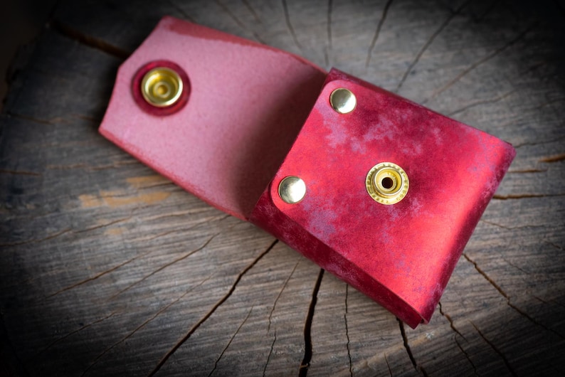 K&ouml;nnte beinhalten: Eine rote Ledertasche mit goldenen Metallschnallen. Die Tasche ist aufgeklappt und zeigt das Innere.