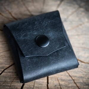 K&ouml;nnte beinhalten: Eine kleine, schwarze Ledertasche mit einem Druckknopfverschluss. Die Tasche hat einen Used-Look und ist aus weichem, geschmeidigem Leder gefertigt.