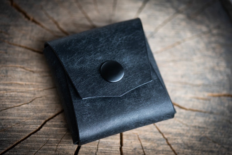 K&ouml;nnte beinhalten: Eine kleine, schwarze Ledertasche mit einem Druckknopfverschluss. Die Tasche hat einen Used-Look und ist aus weichem, geschmeidigem Leder gefertigt.