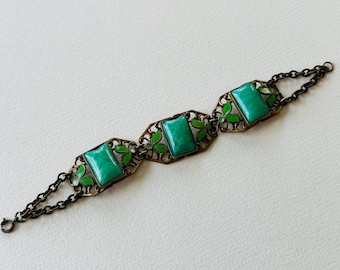 Op de afbeelding: Een vintage armband met drie rechthoekige groene stenen gezet in versierd goudkleurig metaal met een kettingsluiting.