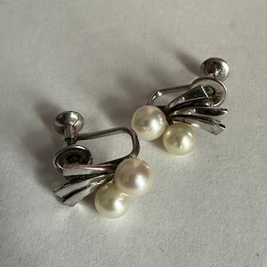 May include: A pair of silver clip-on earrings with three white pearls on each earring.