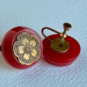 May include: A pair of vintage red screw-back earrings. Each earring has a gold-coloured floral design set in a round, red base. The earrings have a screw-back mechanism for secure wear. A classic accessory.