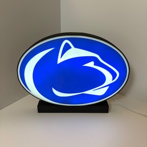 May include: A blue and white oval-shaped light with a white silhouette of a lion's head. The light is on a black base and has a white cord.