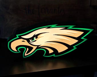 May include: A green and white eagle logo with a black background. The eagle is facing right and has a green outline. The logo is illuminated from behind, creating a glow effect.