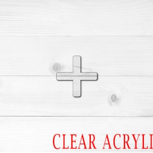 May include: A clear acrylic plus sign on a white wooden background. The text "CLEAR ACRYLIC" is printed in red at the bottom of the image. The plus sign is outlined in black.