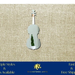 May include: A silver mirror shaped like a violin with a green plant inside. The mirror is on a beige textured background. Multiple Styles & Sizes Available. Fast & Free Shipping! Richstone Arts.