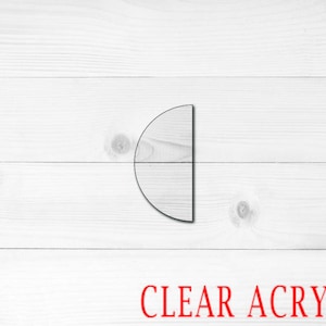 May include: A clear acrylic half circle shape on a white wood background. The text "CLEAR ACRYLIC" is written in red below the shape.