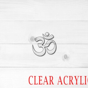 May include: A clear acrylic Om symbol cutout on a white wood background. The text "CLEAR ACRYLIC" is written in red below the symbol.