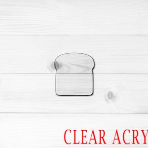 May include: A clear acrylic bread-shaped cookie cutter. The cutter is on a white wood background.