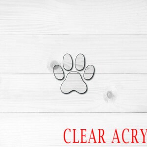 May include: A clear acrylic paw print cutout. The paw print is a simple design with four toes and a pad.