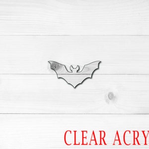 May include: A clear acrylic bat cutout, perfect for Halloween decorations. The bat is shown against a white wood background.