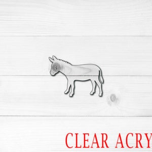 May include: A clear acrylic donkey cutout. The donkey is standing on a white wood background. The text "CLEAR ACRYLIC" is printed in red at the bottom of the image.