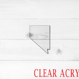 May include: A clear acrylic outline of the state of Nevada on a white wood background. The text "CLEAR ACRYLIC" is printed in red below the state outline.