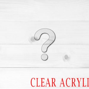 May include: A question mark cut out of clear acrylic. The question mark is on a white wood background. The text "CLEAR ACRYLIC" is written in red below the question mark.