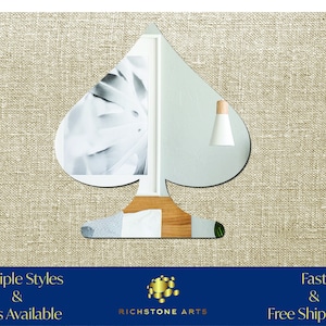 May include: A silver mirror shaped like a spade, reflecting a room with a white lamp and a framed picture. The mirror is on a beige textured surface. Multiple Styles & Sizes Available. Richstone Arts. Fast & Free Shipping!