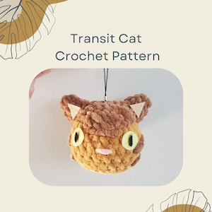 May include: Crochet pattern for a brown and yellow cat with green eyes. The cat is a plush toy and has a black string attached to it. The text "Transit Cat Crochet Pattern" is at the top of the image.