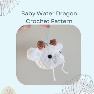 May include: A white crocheted baby water dragon with brown ears and black eyes. The dragon is hanging from a blue string. The text "Baby Water Dragon Crochet Pattern" is above the dragon.