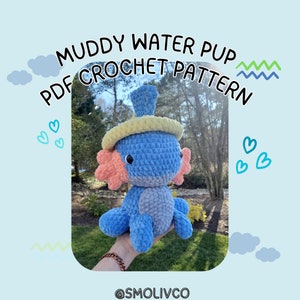 May include: Crochet pattern for a blue and pink axolotl amigurumi toy wearing a yellow hat. The pattern is called "Muddy Water Pup Crochet Pattern".