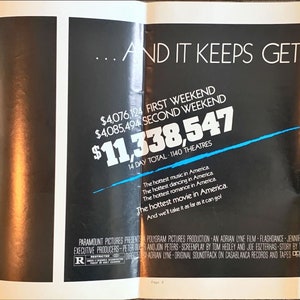 May include: A movie poster for the film "Flashdance" featuring a woman sitting on a ledge. The poster includes the text "...AND IT KEEPS GETTING HOTTER." and the film's box office earnings: "$4,076,124 FIRST WEEKEND", "$4,085,494 SECOND WEEKEND", and "$11,338,547 14 DAY TOTAL 140 THEATRES".