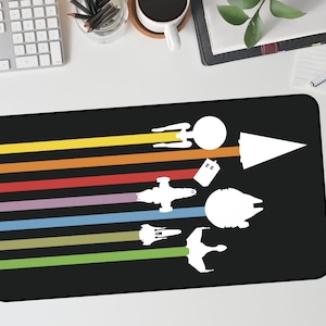 May include: Black rectangular mousepad featuring a colorful design of various spacecraft silhouettes. The design includes a rainbow of horizontal stripes and white spacecraft illustrations, including a spaceship, a TARDIS, and a Millennium Falcon.
