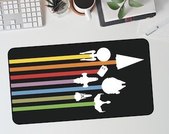 May include: Black rectangular mousepad featuring a colorful design of various spacecraft silhouettes. The design includes a rainbow of horizontal stripes and white spacecraft illustrations, including a spaceship, a TARDIS, and a Millennium Falcon.