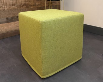 May include: A square, lime green ottoman with a textured fabric cover. The ottoman is sitting on a dark gray floor.