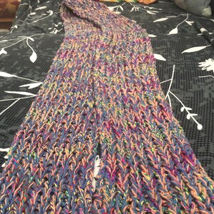 May include: A long, multi-colored knitted scarf with a textured pattern. The scarf is made with a variety of shades of blue, pink, and green yarn.