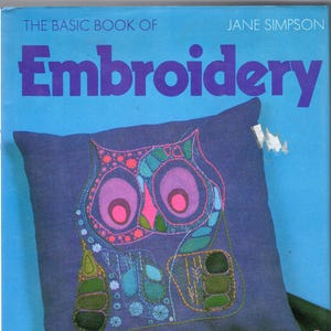 May include: The cover of a book titled "The Basic Book of Embroidery" by Jane Simpson. It shows a cushion with an embroidered owl design in shades of pink, purple, green, and blue. Embroidery supplies, including scissors and thread, are also visible.