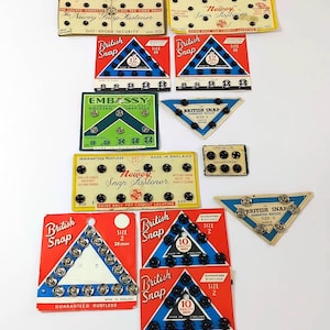 May include: A selection of vintage packaging for British snap fasteners, showcasing different sizes and colours. The packaging features the brand names "British Snap" and "Newey Snap Fastener".