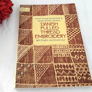 May include: A vintage book titled "Danish Pulled Thread Embroidery" with English and Danish text. The cover has a brown and beige geometric pattern. The book is part of the Dover Needlework Series.