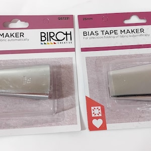 May include: Two silver bias tape makers in clear plastic packaging. The packaging is white and pink with the text "BIAS TAPE MAKER" and "BIRCH CREATIVE". One maker is 18mm, the other is 25mm.