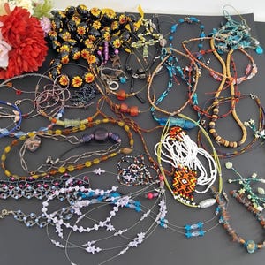 May include: A selection of necklaces in diverse styles and colours, including beaded, chain, and pendant designs. The necklaces feature various materials, such as glass beads, metal chains, and colourful stones. Some necklaces have floral and star-shaped accents.