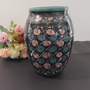 May include: A black ceramic vase with a teal rim and a geometric pattern of white lines, pink and teal circles.