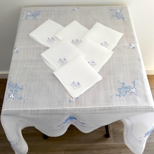 May include: A white tablecloth with blue embroidered floral designs and a set of six white napkins with blue embroidered designs.