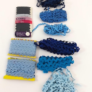 May include: A selection of blue ric-rac trim in shades of navy, light blue, and turquoise. Some trim is on yellow spools, while other pieces are loose. One package of black ric-rac is visible, with the brand name "Coats" and the text "polyester ric-rac".