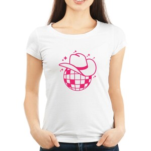 Pu&ograve; includere: Una maglietta bianca con un design a forma di palla da discoteca rosa. La palla da discoteca ha un cappello da cowboy rosa in cima.