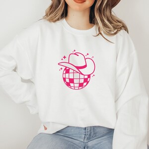 Pu&ograve; includere: Felpa bianca con una grafica rosa di una palla da discoteca che indossa un cappello da cowboy.